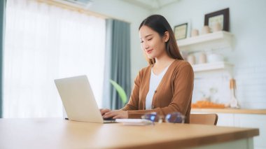 Ev mutfağında dizüstü bilgisayarla çalışan güzel bir Asyalı kadın. Evde çalış.