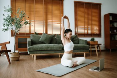 Mutlu genç Asyalı kadın yoga ve omuz egzersizi yapıyor. Oturma odasında yerde oturuyor.