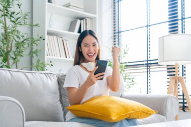 Happy young asian woman relax on comfortable couch at home texting messaging on smartphone, smiling girl use cellphone, chatting online message, shopping online from home