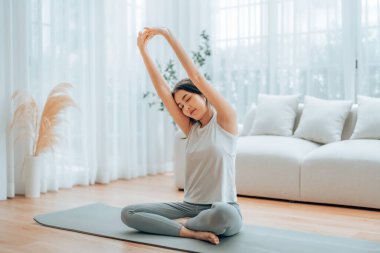 Mutlu genç Asyalı kadın yoga ve omuz egzersizi yapıyor. Oturma odasında yerde oturuyor.