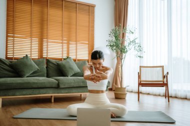 Mutlu genç Asyalı kadın yoga ve omuz egzersizi yapıyor. Oturma odasında yerde oturuyor.