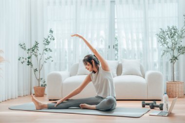 Mutlu genç Asyalı kadın yoga ve omuz egzersizi yapıyor. Oturma odasında yerde oturuyor.