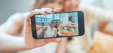 İki genç Asyalı kadın gülümseyip mutlu olurken evlerindeki oturma odalarında fotoğraf çektirip kameraya bakıyorlar.