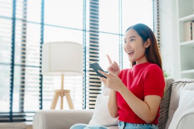 Happy young asian woman relax on comfortable couch at home texting messaging on smartphone, smiling girl use cellphone, chatting online message, shopping online from home