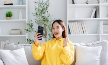 Happy young asian woman relax on comfortable couch at home texting messaging on smartphone, smiling girl use cellphone, chatting online message, shopping online from home
