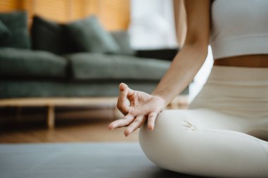 Evde yoga ve meditasyon yapan Asyalı bir kadının lotus pozisyonunda oturma odasında oturduğu eli yakın. Dikkatli meditasyon ve refah kavramı