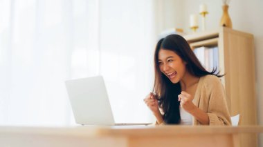 Asyalı bir kadının kazanmasını ya da bilgisayar laptopunda ecommerce alışveriş teklifi almasını kutlayan komik bir coşku. Heyecanlı mutlu kız kazanan başarıyı kutlayan deftere bakıyor.