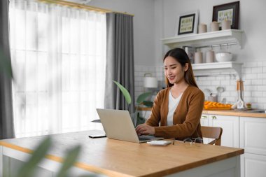Ev mutfağında dizüstü bilgisayarla çalışan güzel bir Asyalı kadın. Evde çalış.
