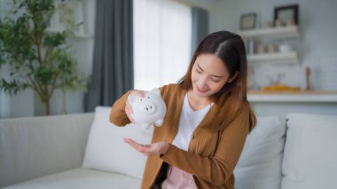 Genç Asyalı kadın kumbaraya para koyuyor. Para ve mali yatırım tasarrufu