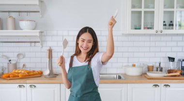 Genç Asyalı kadın mutfakta dans ediyor. Güzel bir kadının hafta sonu boş zamanlarında evde dinlenmesinin keyfi.