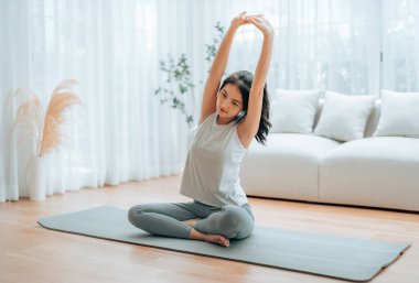 Mutlu genç Asyalı kadın yoga ve omuz egzersizi yapıyor. Oturma odasında yerde oturuyor.