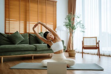 Mutlu genç Asyalı kadın yoga ve omuz egzersizi yapıyor. Oturma odasında yerde oturuyor.