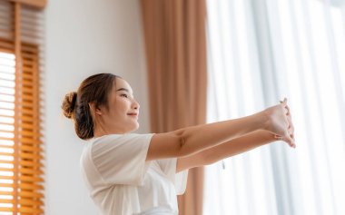 Genç Asyalı güzel kadın sabahları evde esneme hareketleri yapıyor. Sağlık ve vücut bakımı kavramı