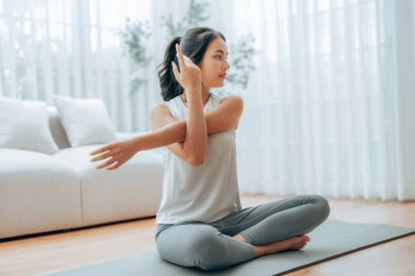 Mutlu genç Asyalı kadın yoga ve omuz egzersizi yapıyor. Oturma odasında yerde oturuyor.