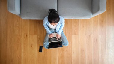 Asya 'lı genç bir kadının oturma odasında cep telefonuyla bilgisayarda çalışırken en iyi görüntüsü.