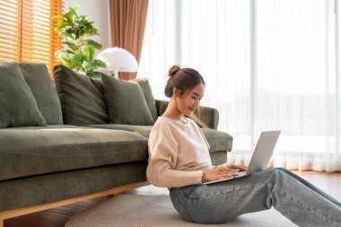Genç Asyalı güzel bir kadın rahat koltukta dinleniyor, evinde dizüstü bilgisayar kullanıyor, sosyal ağda arkadaşlarıyla sohbet eden mutlu bir kız, haftasonunu, film izleyerek, online alışveriş yaparak geçiriyor.