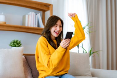 Happy young asian woman relax on comfortable couch at home texting messaging on smartphone, smiling girl use cellphone, chatting online message, shopping online from home