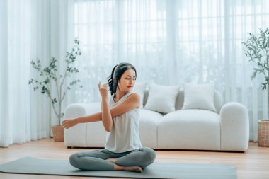 Mutlu genç Asyalı kadın yoga ve omuz egzersizi yapıyor. Oturma odasında yerde oturuyor.