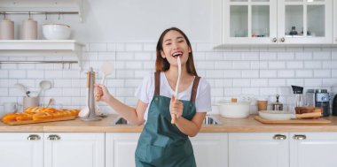 Genç Asyalı kadın mutfakta dans ediyor. Güzel bir kadının hafta sonu boş zamanlarında evde dinlenmesinin keyfi.