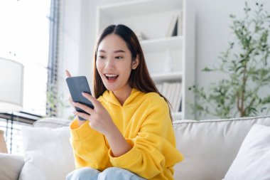 Happy young asian woman relax on comfortable couch at home texting messaging on smartphone, smiling girl use cellphone, chatting online message, shopping online from home