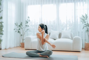 Mutlu genç Asyalı kadın yoga ve omuz egzersizi yapıyor. Oturma odasında yerde oturuyor.