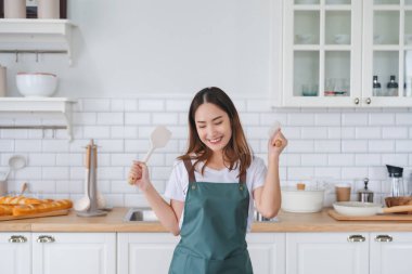 Genç Asyalı kadın mutfakta dans ediyor. Güzel bir kadının hafta sonu boş zamanlarında evde dinlenmesinin keyfi.