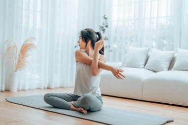 Mutlu genç Asyalı kadın yoga ve omuz egzersizi yapıyor. Oturma odasında yerde oturuyor.
