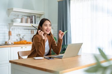 Ev mutfağında dizüstü bilgisayarla çalışan güzel bir Asyalı kadın. Evde çalış.