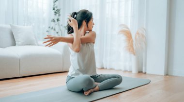 Mutlu genç Asyalı kadın yoga ve omuz egzersizi yapıyor. Oturma odasında yerde oturuyor.