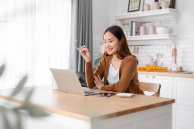 Ev mutfağında dizüstü bilgisayarla çalışan güzel bir Asyalı kadın. Evde çalış.