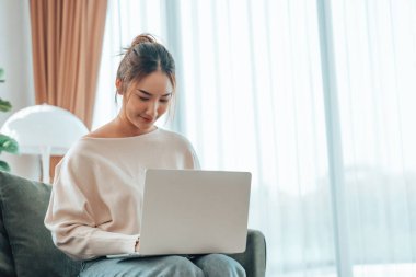 Genç Asyalı güzel bir kadın rahat koltukta dinleniyor, evinde dizüstü bilgisayar kullanıyor, sosyal ağda arkadaşlarıyla sohbet eden mutlu bir kız, haftasonunu, film izleyerek, online alışveriş yaparak geçiriyor.