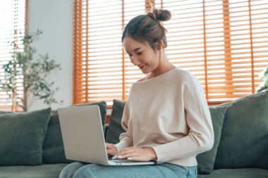 Genç Asyalı güzel bir kadın rahat koltukta dinleniyor, evinde dizüstü bilgisayar kullanıyor, sosyal ağda arkadaşlarıyla sohbet eden mutlu bir kız, haftasonunu, film izleyerek, online alışveriş yaparak geçiriyor.