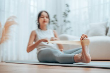 Genç Asyalı kadın pilates egzersizi yapıyor. Kapalı alandaki yoga minderinde omuz çalışması için elastik kayışı kullanarak kollarını çekiyor. Evde direniş bandı egzersizi