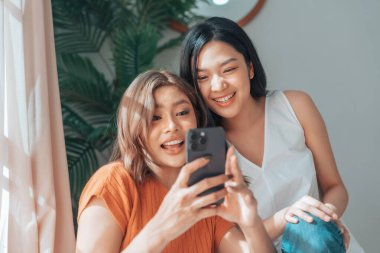 İki genç Asyalı kadın gülümseyip mutlu olurken evlerindeki oturma odalarında selfie çekiyorlar. Video görüşmesi, toplantı konferansı, kameraya bakıyorlar.