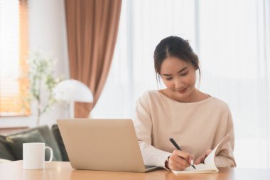 Genç Asyalı kadın mutlu, pozitif, güzel iş kadını. Oturma odasında dizüstü bilgisayar kullanarak oturuyor.