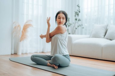 Mutlu genç Asyalı kadın yoga ve omuz egzersizi yapıyor. Oturma odasında yerde oturuyor.