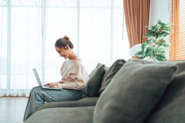 Genç Asyalı güzel bir kadın rahat koltukta dinleniyor, evinde dizüstü bilgisayar kullanıyor, sosyal ağda arkadaşlarıyla sohbet eden mutlu bir kız, haftasonunu, film izleyerek, online alışveriş yaparak geçiriyor.