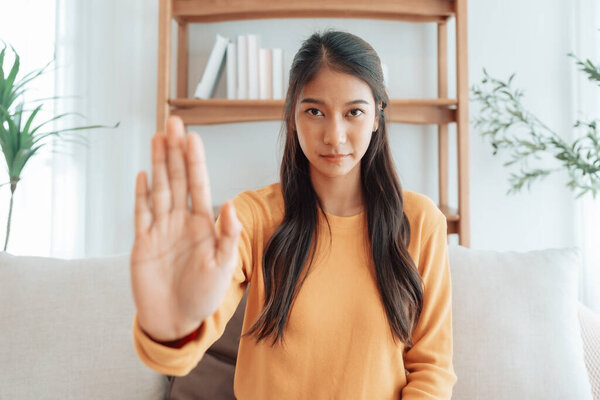Young Asian woman with serious expression raising her hand stop gesture. Concept of protest against harassment, discrimination, and violation of human rights. Symbol of resistance and social justice
