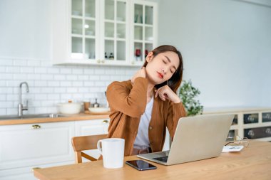 Ofis sendromu konsepti. Bilgisayarda uzun süre çalıştıktan sonra boyun ve omuz ağrısı çeken Asyalı genç bir kadın. Kaslarını gevşetmek için esniyor.