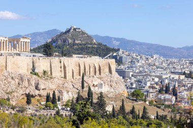 Atina, Yunanistan - 17 Ekim 2022: Muse Tepesi 'nden mavi gökyüzünün arka planında Atina Akropolis manzarası. Uzakta şehrin ve Lycabettus Dağı 'nın havadan görünüşü