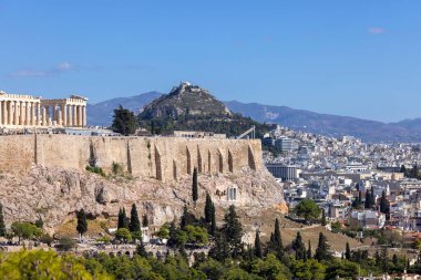 Atina, Yunanistan - 17 Ekim 2022: Muse Tepesi 'nden mavi gökyüzünün arka planında Atina Akropolis manzarası. Uzakta şehrin ve Lycabettus Dağı 'nın havadan görünüşü