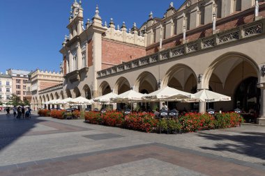Krakow, Polonya - 6 Eylül 2023: Rönesans Ortaçağ Kuaför Salonu (Sukiennice) Eski Şehir 'in ana meydanında yer almaktadır. Binanın önünde şemsiyeli açık hava restoranı