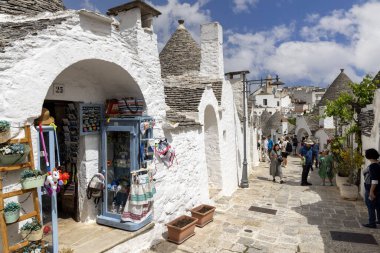 Alberobello, Apulia, İtalya - 21 Mayıs 2024: Trulli evleri, geleneksel, eşsiz, konik çatısı olan Apulian kuru taş barakası. Tarihi bir kasabanın caddelerinden birinde yürüyen turistler