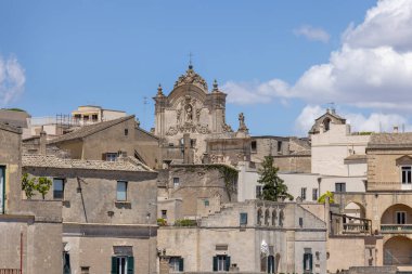 İtalya, Matera - 22 Mayıs 2024: Matera 'nın Sassi kayasına oyulmuş tarihi şehir manzarası. Uzak bir mesafede Assisi 'li Aziz Francis Barok Kilisesi