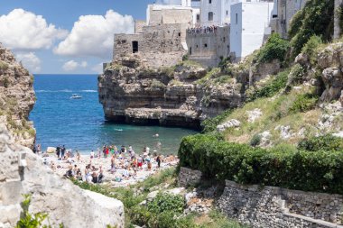 Polignano a Mare, Italy, Apulia - May 24, 2024: Lama Monachile beach, located between picturesque cliffs by Adriatic Sea. People relaxing on stone shore and swimming in the water clipart