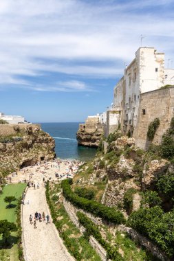 Polignano a Mare, İtalya, Apulia - 24 Mayıs 2024: Adriyatik Denizi kıyısındaki kayalıklar arasında yer alan Lama Monachile plajı. Taş sahilde dinlenen ve suda yüzen insanlar.