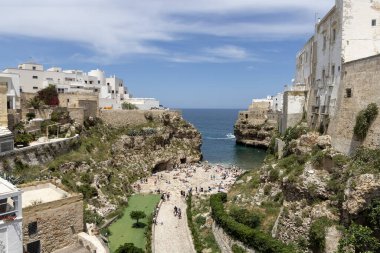 Polignano a Mare, İtalya, Apulia - 24 Mayıs 2024: Adriyatik Denizi kıyısındaki kayalıklar arasında yer alan Lama Monachile plajı. Taş sahilde dinlenen ve suda yüzen insanlar.