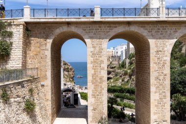 Polignano a Mare, İtalya, Apulia - 24 Mayıs 2024: Adriyatik Denizi kıyısındaki pitoresk kayalıklar arasında yer alan Lama Monachile sahilindeki Bourbon Köprüsü (Ponte Borbonico)