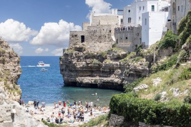 Polignano a Mare, İtalya, Apulia - 24 Mayıs 2024: Adriyatik Denizi kıyısındaki kayalıklar arasında yer alan Lama Monachile plajı. Taş sahilde dinlenen ve suda yüzen insanlar.