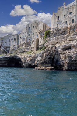 Polignano a Mare, İtalya, Apulia - 24 Mayıs 2024: Kayalıklar üzerine inşa edilen binalar, resimli kaya ve mağaraların manzarası. Kayalık sahil boyunca tekne gezisi büyük bir turistik cazibedir.